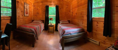 A cabin with two wooden beds, a small table with a lamp, and a guitar.