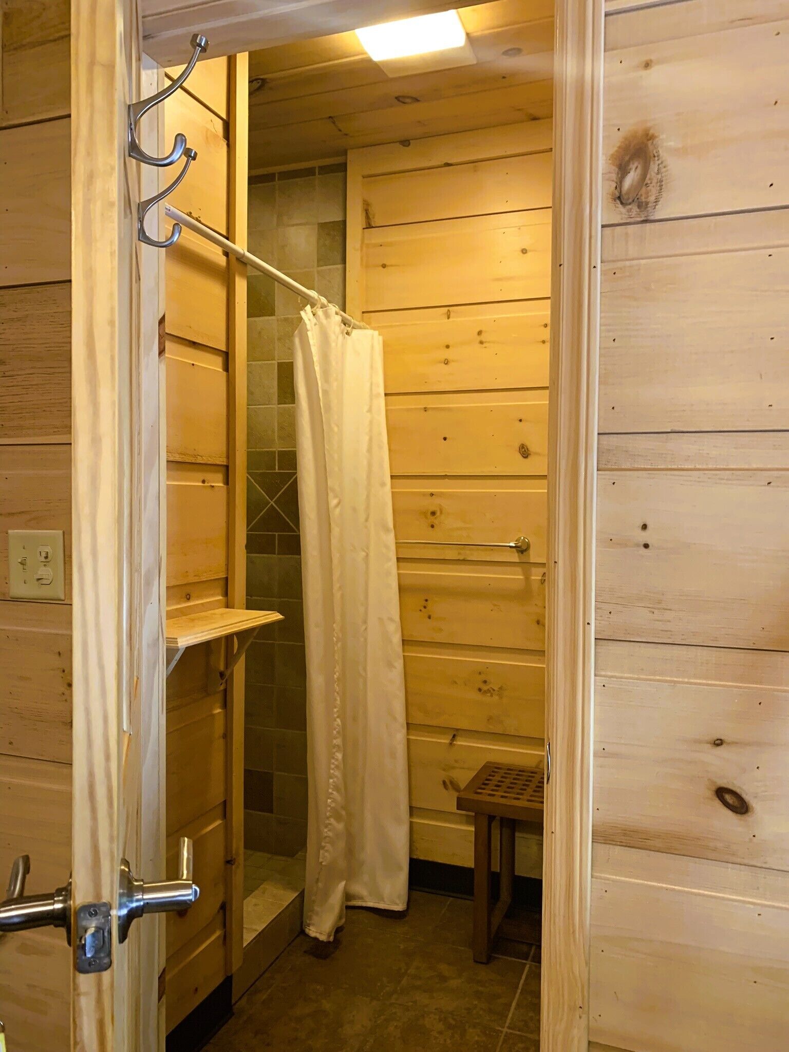 A wooden cabin bathroom with a shower curtain, a wooden bench, and a towel rack.