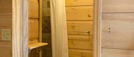 Een houten badkamer met een douchegordijn, een houten bankje en een handdoekhouder.