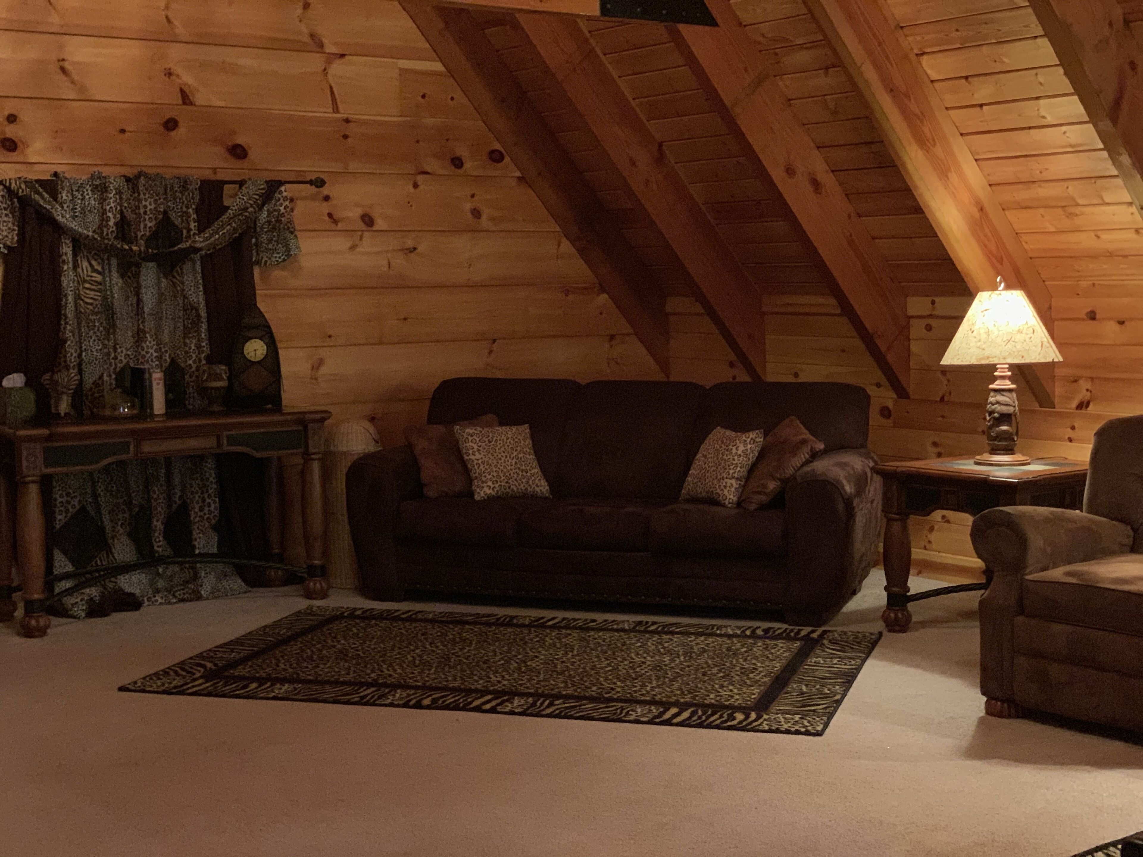 Ein gemütliches Zimmer mit einem dunkelbraunen Sofa, einem gemusterten Teppich, einer Lampe und Holzwänden.