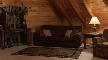 Ein gemütliches Zimmer mit einem dunkelbraunen Sofa, einem gemusterten Teppich, einer Lampe und Holzwänden.