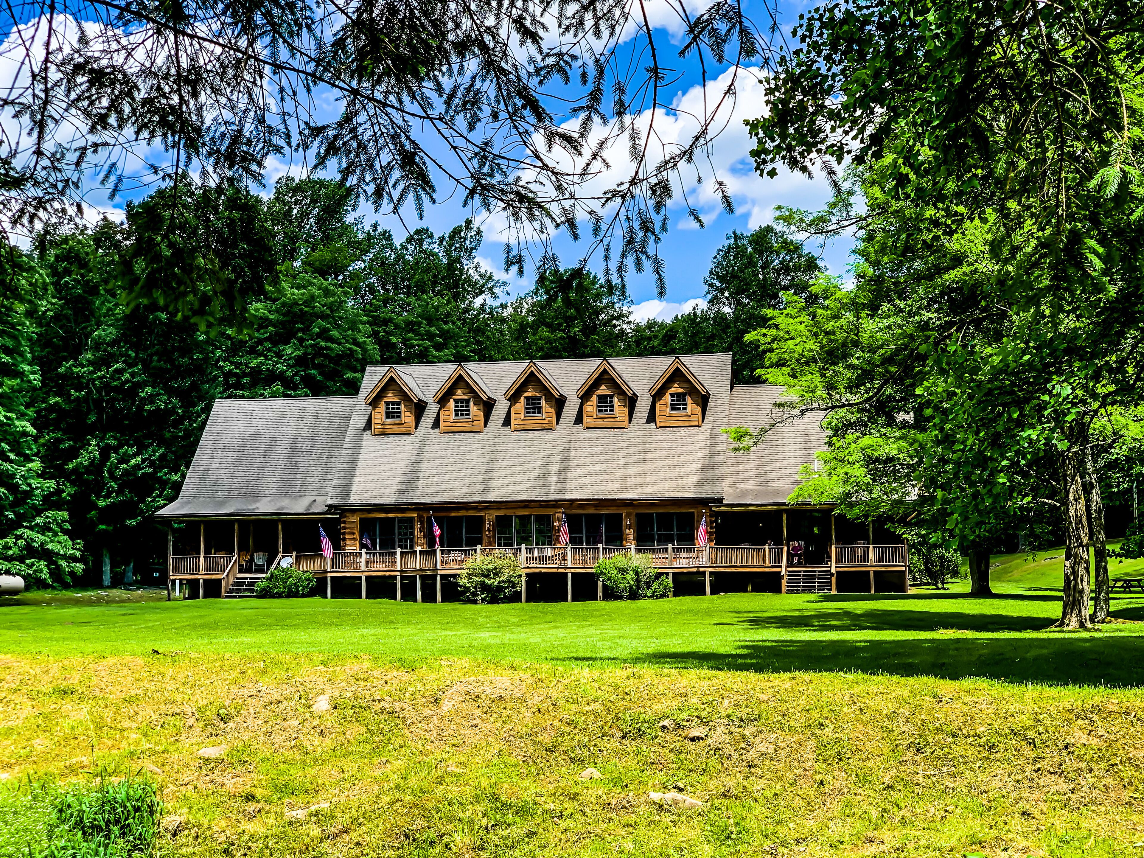A lodge with a large porch and multiple windows, surrounded by lush greenery and trees.