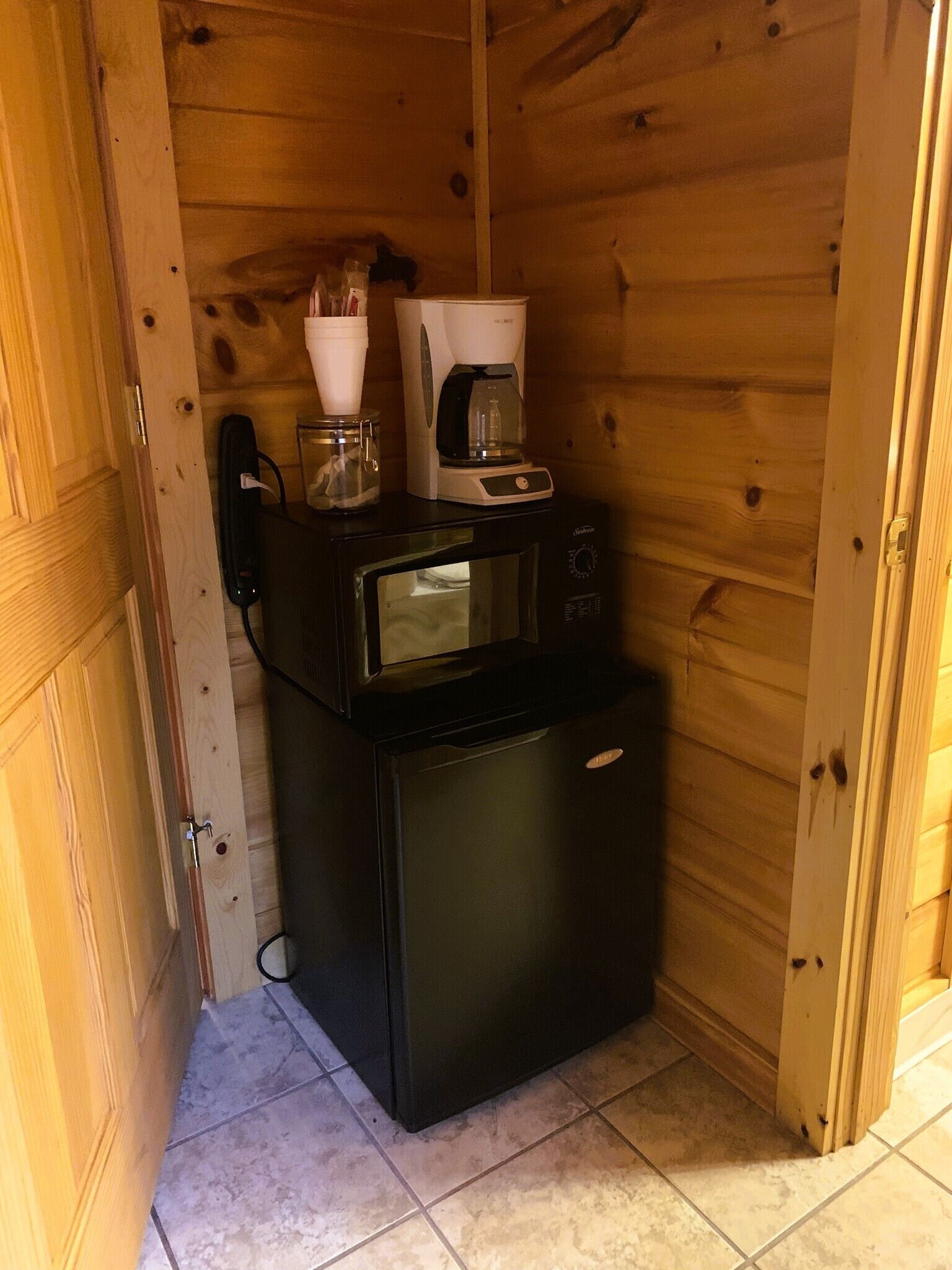A compact kitchenette with a microwave, coffee maker, and a glass container on the counter.