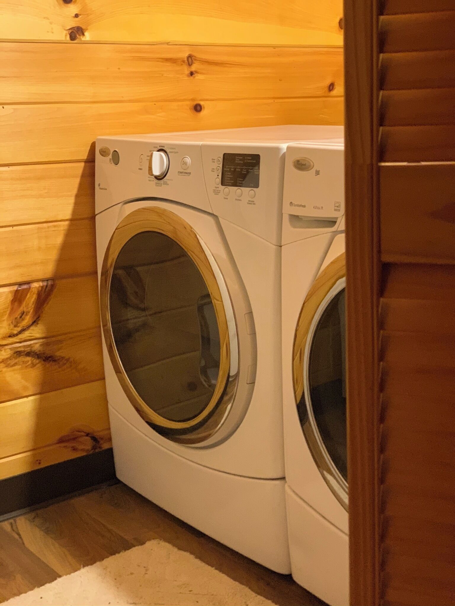 A front-loading washing machine in a room with wooden walls and a carpeted floor.