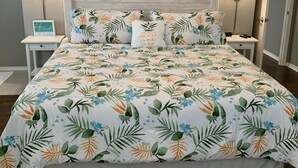 Une chambre à coucher avec une couvre-lit à motifs floraux, deux lampes de chevet, un élément décoratif mural et une petite table de chevet avec une horloge.