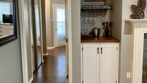Un couloir doté d’un plancher en bois mène à une cuisine avec des armoires blanches et un comptoir.