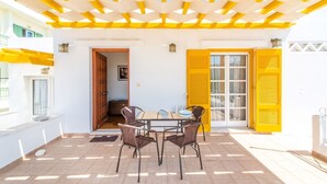 A patio with a table and chairs, a yellow pergola, and a door with yellow shutters. - Spacious house with terrace combining tradition and modernity near sandy beach (Tinos)