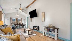 Un salon comprenant un canapé, une table basse, un téléviseur, une cheminée et un coin repas avec des chaises et une table.