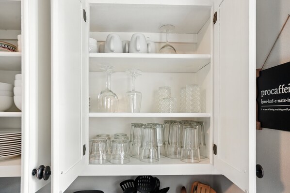 A white cabinet with shelves containing various glassware, including wine glasses and tumblers. - 3BR Near DT, BOK, Greenwood | Gathering Pl 5 miles (Tulsa)