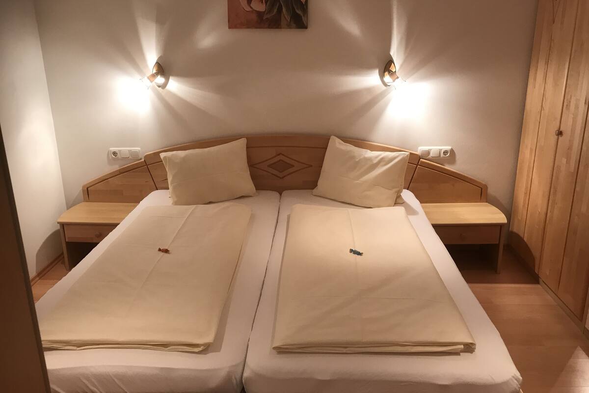 Una cama doble con dos almohadas, cabecero de madera, mesitas de noche e iluminación en la pared.