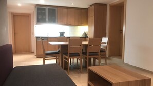 Un espacio habitable compacto con kitchenette, una zona de comedor con cuatro sillas, un sofá y una pequeña mesa de madera.