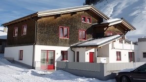 Un chalet de dos pisos con ventanas de marco rojo y techo inclinado, rodeado de nieve.