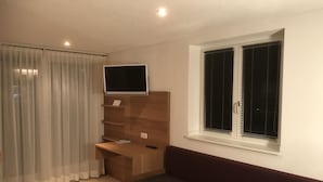 Una habitación moderna con cama, escritorio, televisión y ventana con persianas.