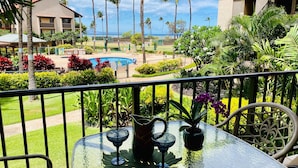 Un balcon avec une table en verre, deux chaises et un pot de fleurs.