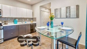 A modern kitchen with a glass dining table, stainless steel appliances, and a stone backsplash. - Sleek Modern 4BR Near Fort Bliss (El Paso)