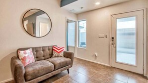 A living room with a brown leather sofa, a round mirror, and a door with frosted glass panels. - Sleek Modern 4BR Near Fort Bliss (El Paso)