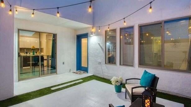 A modern outdoor patio with string lights, a seating area with cushions, and a view of the interior through glass doors. - Sleek Modern 4BR Near Fort Bliss (El Paso)