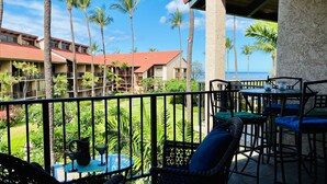A balcony with outdoor furniture, palm trees, and a view of a building with a red roof. - Two Bedroom Deluxe Partial Ocean View Luana Kai Resort B304 (Kihei)