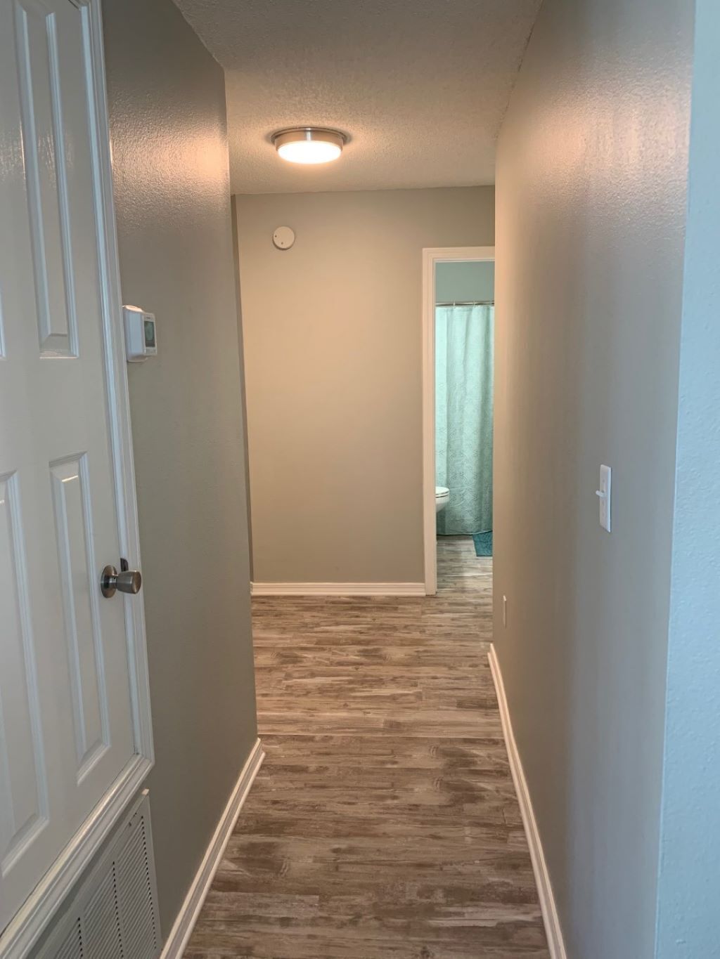 A narrow hallway with wooden flooring, white walls, and a ceiling light.