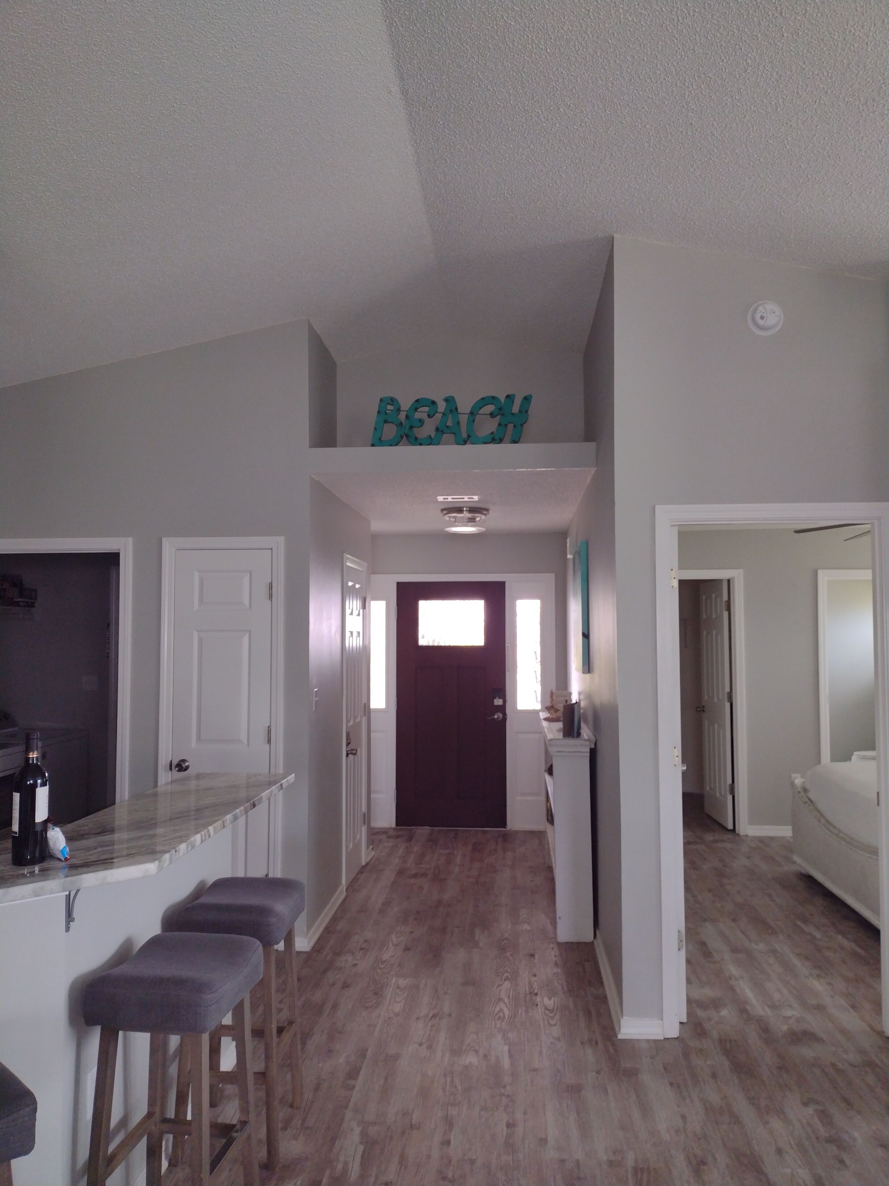 Un couloir avec un plancher en bois, un coin bar avec des tabourets et une enseigne sur laquelle on peut lire « PLAGE ».