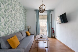 A living room with a grey sofa, a wooden coffee table, a TV mounted on the wall, and a window with curtains. - Tetuán 4D - One Bedroom Apartment, Sleeps 4 (Sevilla)