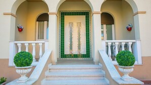A building entrance with a green tiled door, white balustrades, and two potted topiary plants. - Villa Mimosa - Apt 2 (Desenzano del Garda)