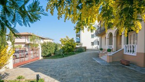 A paved courtyard with a clear sky, surrounded by buildings with balconies and a gated entrance. - Villa Mimosa - Apt 2 (Desenzano del Garda)