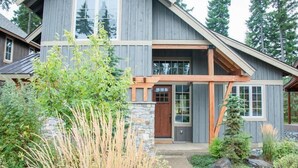 Une maison à deux étages, avec des fondations en pierre, des poutres en bois et une grande véranda à l’avant.