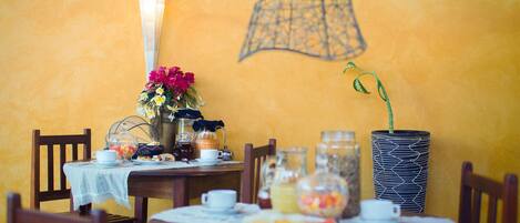 A dining table set with a vase of flowers, a coffee pot, and various food items.