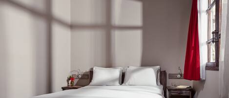 Un dormitorio ordenado con cama, mesitas de noche y una ventana con cortinas.