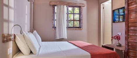 A bedroom with a bed, a window with curtains, a bedside table with a vase, and a wooden door.