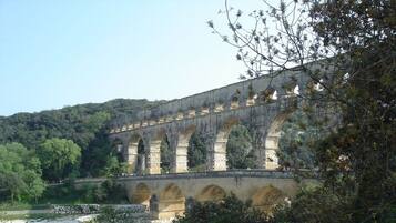 A stone aqueduct with multiple arches, surrounded by lush greenery and a river below.