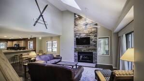 A spacious living area with a stone fireplace, a large TV mounted on the wall, and a ceiling fan.