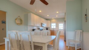 Une cuisine spacieuse avec des meubles blancs, une table à manger avec des chaises et un ventilateur de plafond.