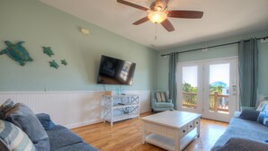 Un salon doté d’un ventilateur de plafond, d’un téléviseur à écran plat, d’une table basse blanche et d’un canapé.