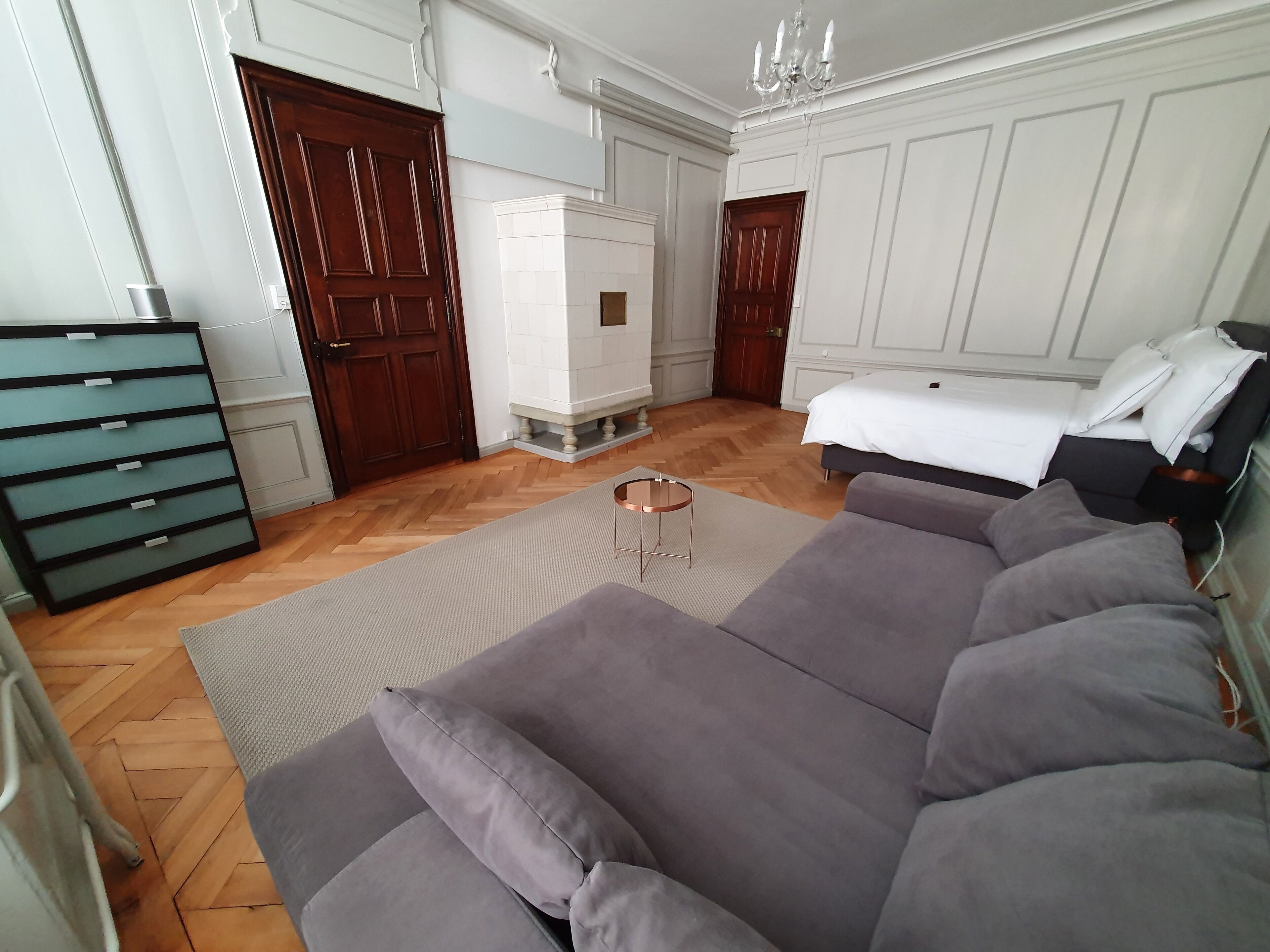 A bedroom with a large grey sofa, a small round table, and a white wardrobe.