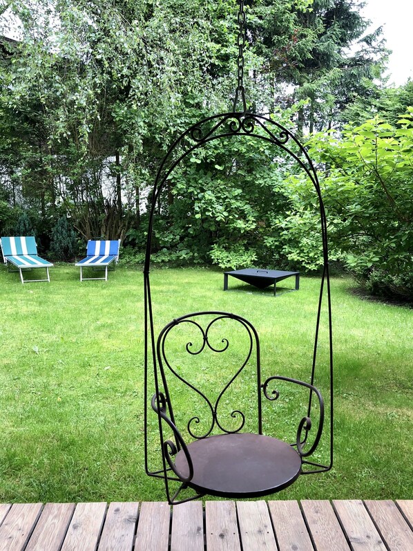 Un giardino con un'amaca, due poltrone a righe e una panchina.