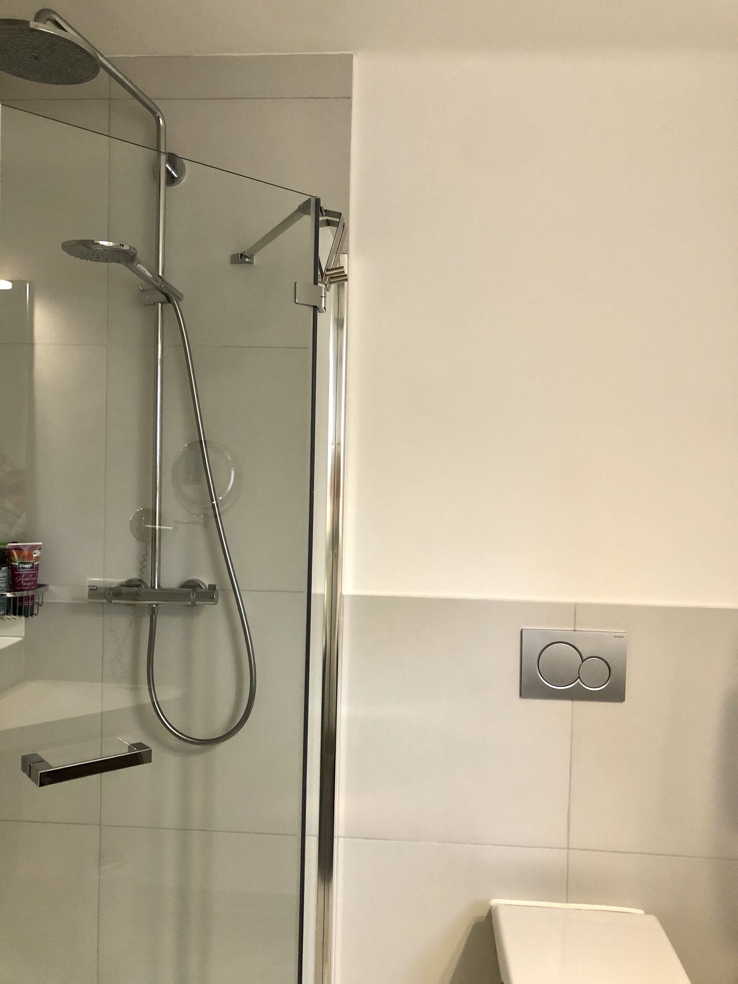 Una ducha moderna con cerramiento de vidrio, cabezal de ducha de mano y panel de control en la pared.