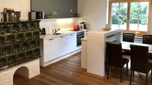 A modern kitchen with white cabinetry, a built-in oven, and a dining area with a table and chairs.
