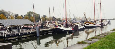Un puerto deportivo con varias embarcaciones amarradas, un paseo techado y una zona verde a orillas del agua.