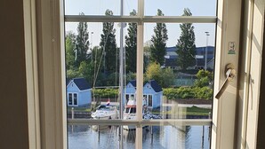 Ein Schlafzimmer mit einem großen Fenster mit Blick auf ruhiges Wasser, auf dem Boote und Häuser schwimmen.