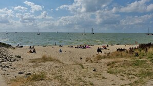 Ein Strand mit badenden Menschen, Booten auf dem Wasser und einem klaren Himmel.