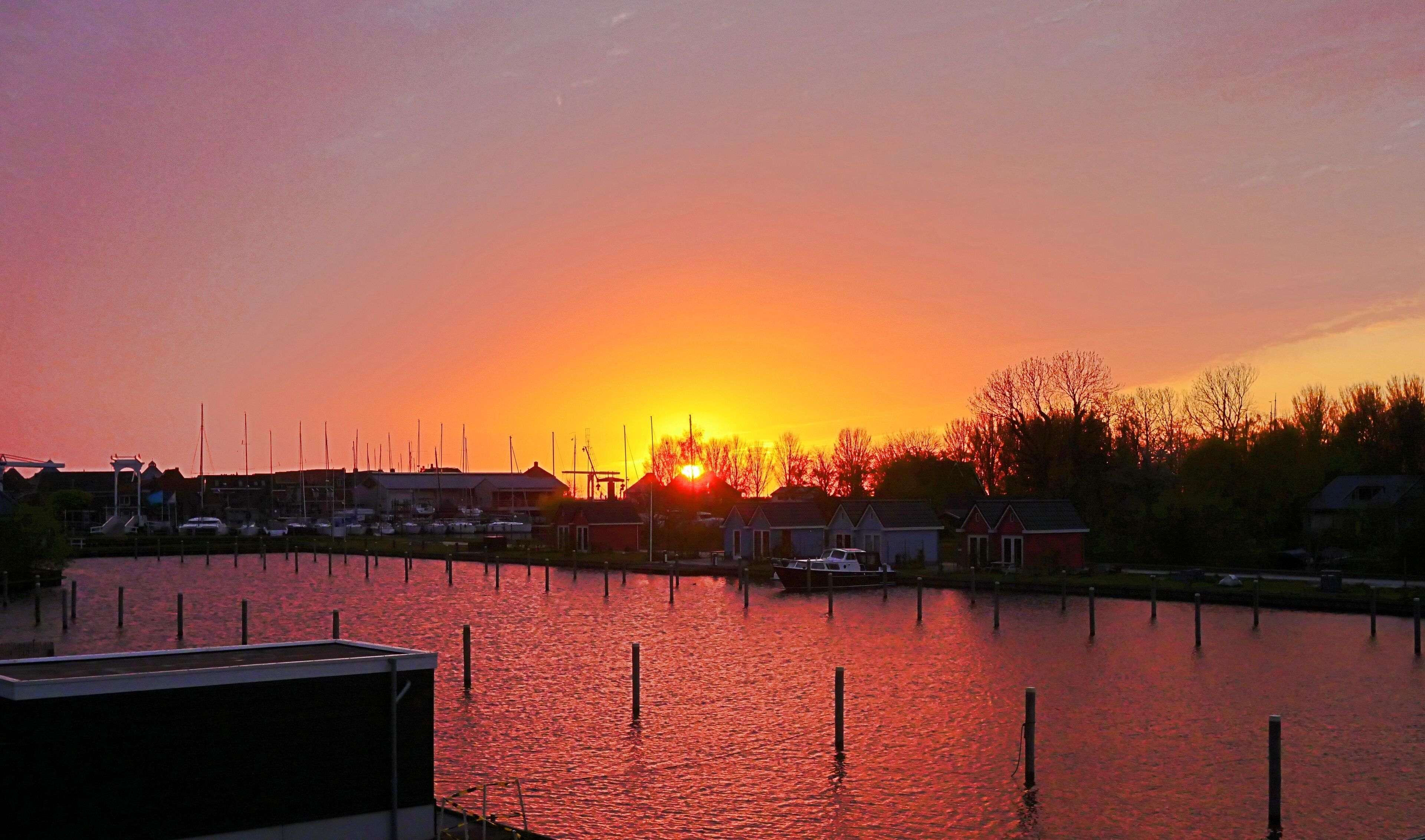 A marina at sunset with boats docked and a calm water surface.