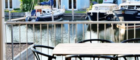A view of a marina with boats docked, a wooden deck with chairs, and houses in the background.