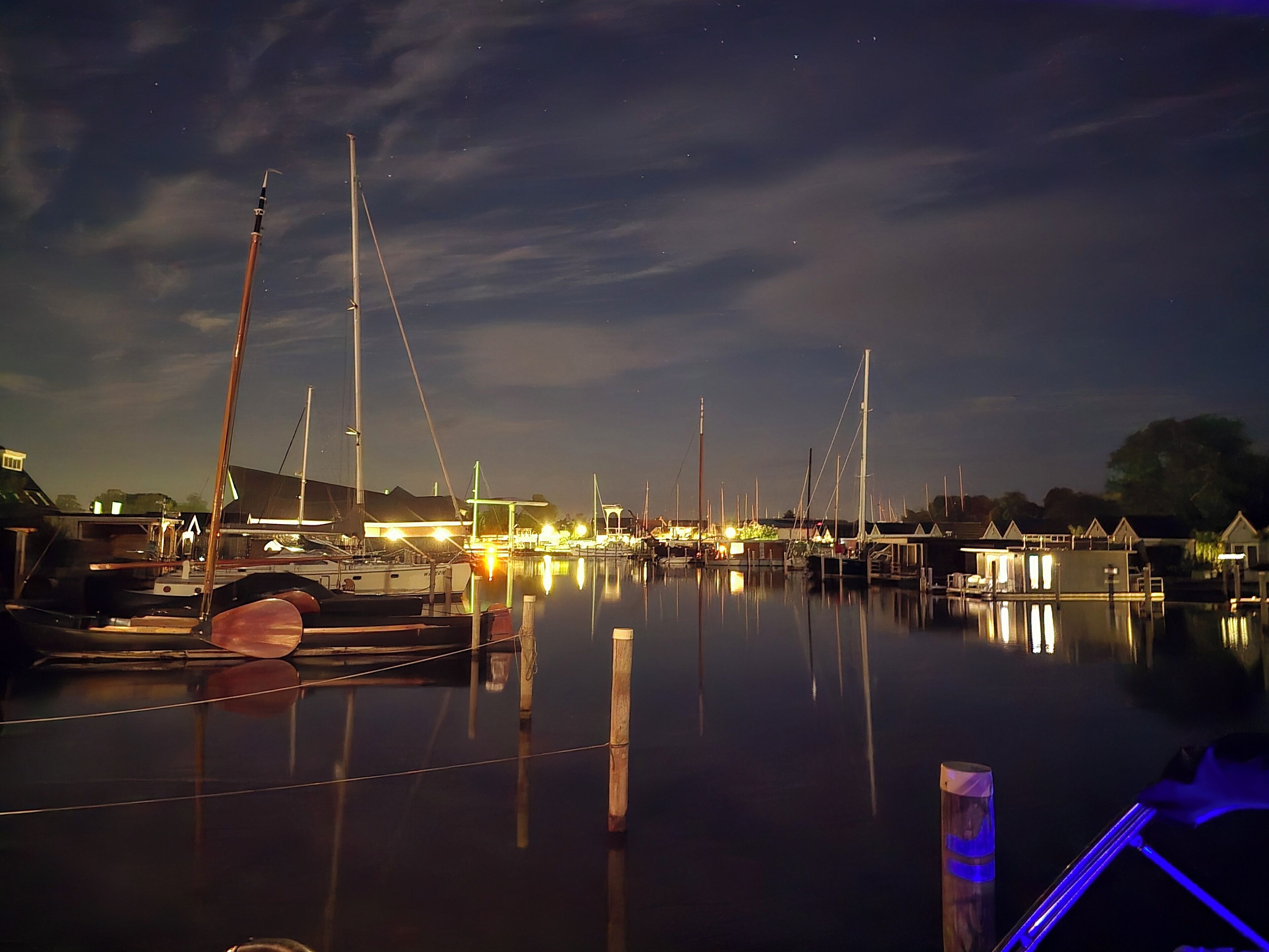 Un port de plaisance de nuit, avec des bateaux amarrés et une eau calme qui reflète les lumières.