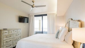 A bedroom with a large bed, a ceiling fan, a television on the wall, and a view of the outdoors through a window. - Summer House 201B | Beach views and deck access from every room! (Orange Beach)