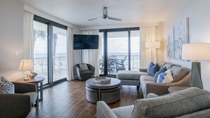 A modern living room with a flat-screen TV, comfortable seating, a round coffee table, and a balcony with a view. - Summer House 201B | Beach views and deck access from every room! (Orange Beach)