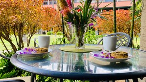 Una mesa redonda de vidrio con dos tazas blancas y platos de galletas, rodeada de follaje otoñal.