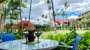 A round glass table with two blue chairs, a decorative pitcher, and a glass on a woven mat. - One Bedroom Deluxe Garden View Launa Kai Resort C109 (Kihei)