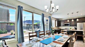 A modern kitchen with a dining area, large windows, and a view of the outdoors.